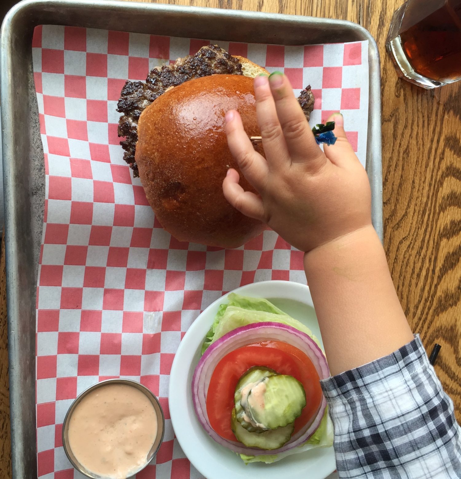 A child reaching for a burger on a tray.