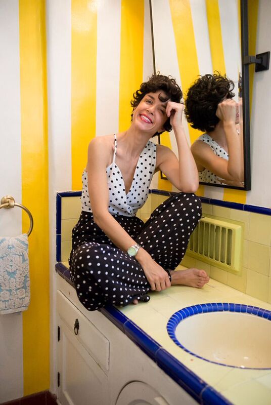 A woman sitting on a sink in a yellow and white bathroom.