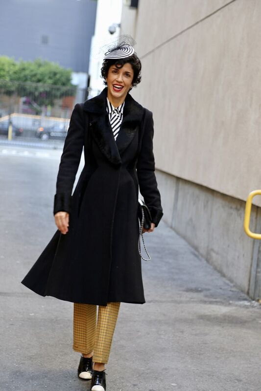 A woman in a black coat and gold pants walking down the street.