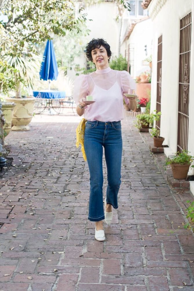 A woman wearing a pink top and jeans walking down a brick walkway.