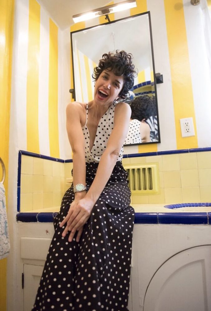 A woman in a polka dot dress sitting on a sink in a bathroom.