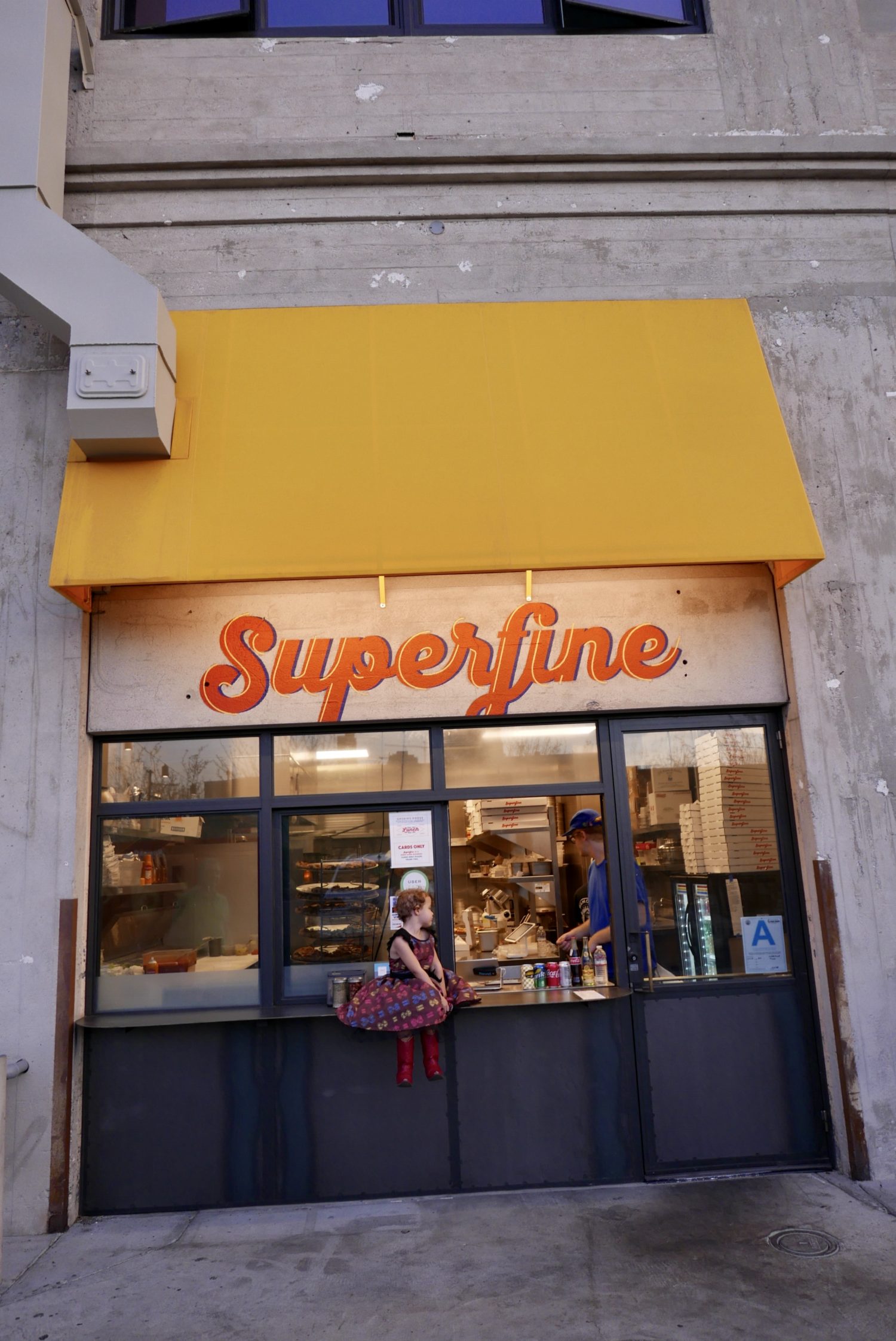 A man is standing in front of a Superfine Pizza store.
