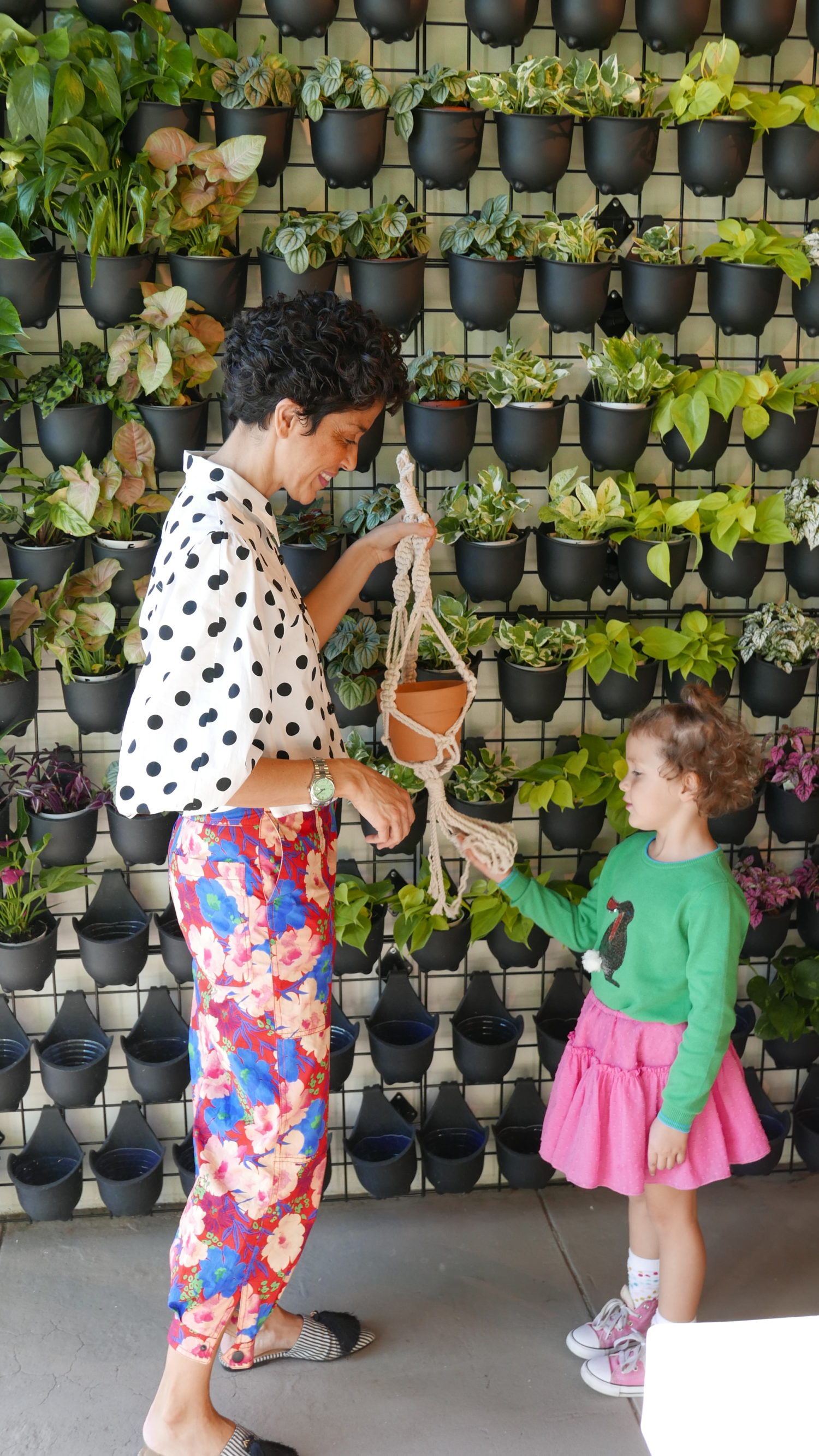 A woman and a little girl standing in front of a Le Petit Garden wall.